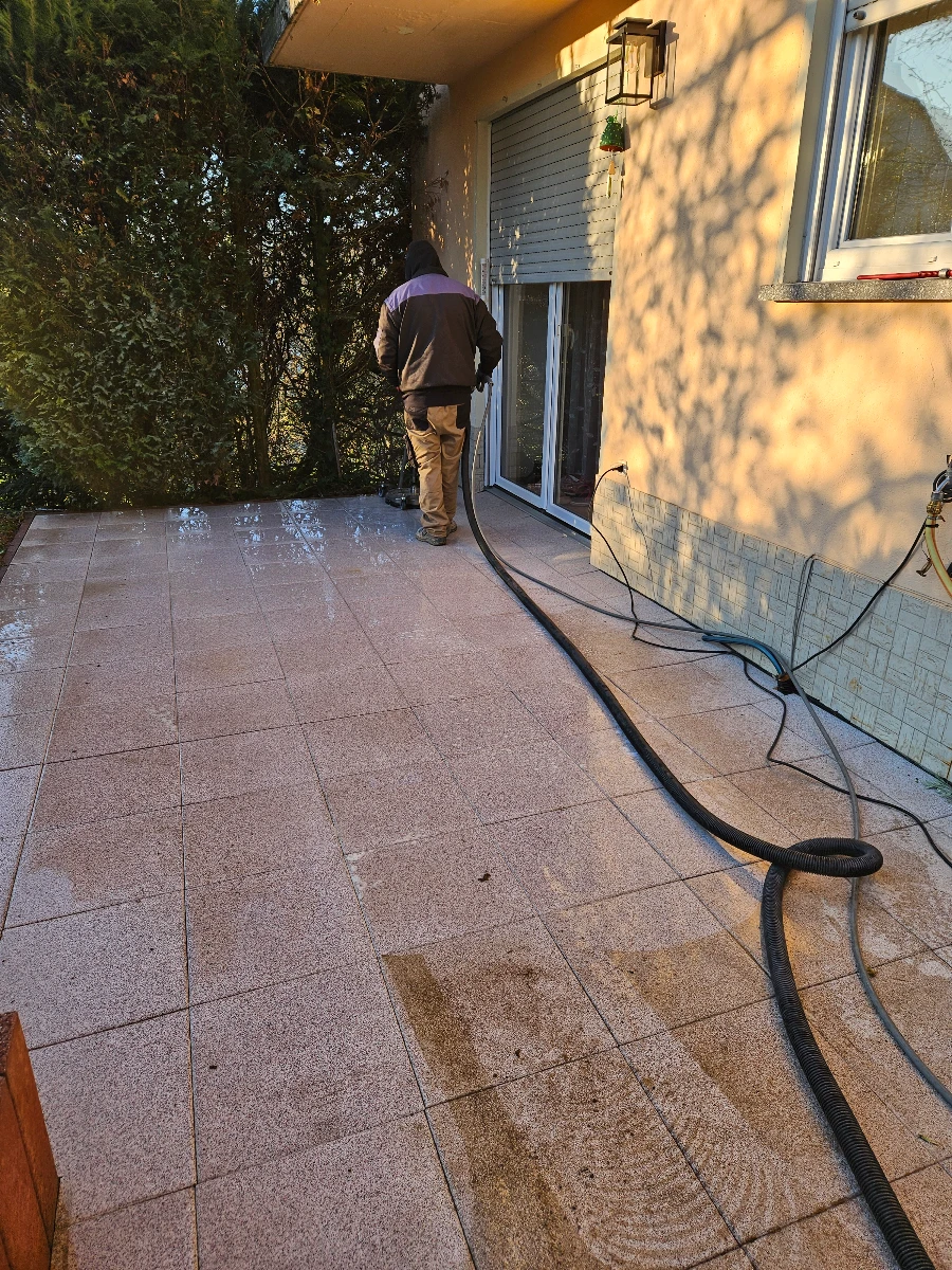 Fachkraft bei Terrassenreinigung einer gefliesten Außenterrasse mit Hochdruckreiniger vor Hausfassade