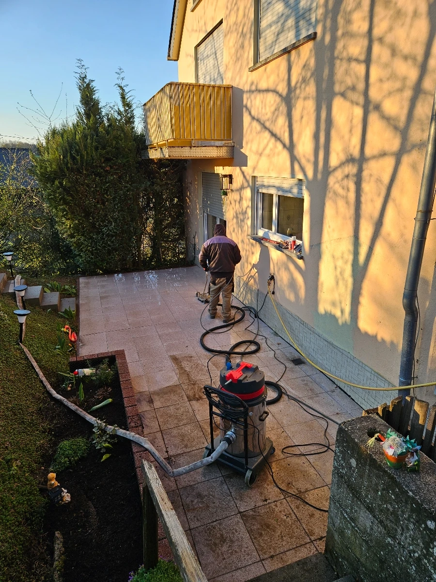 Techniker führt Terrassenreinigung auf hellen Terrassenplatten vor Hausfassade mit professionellem Nass-/Trockensauger durch
