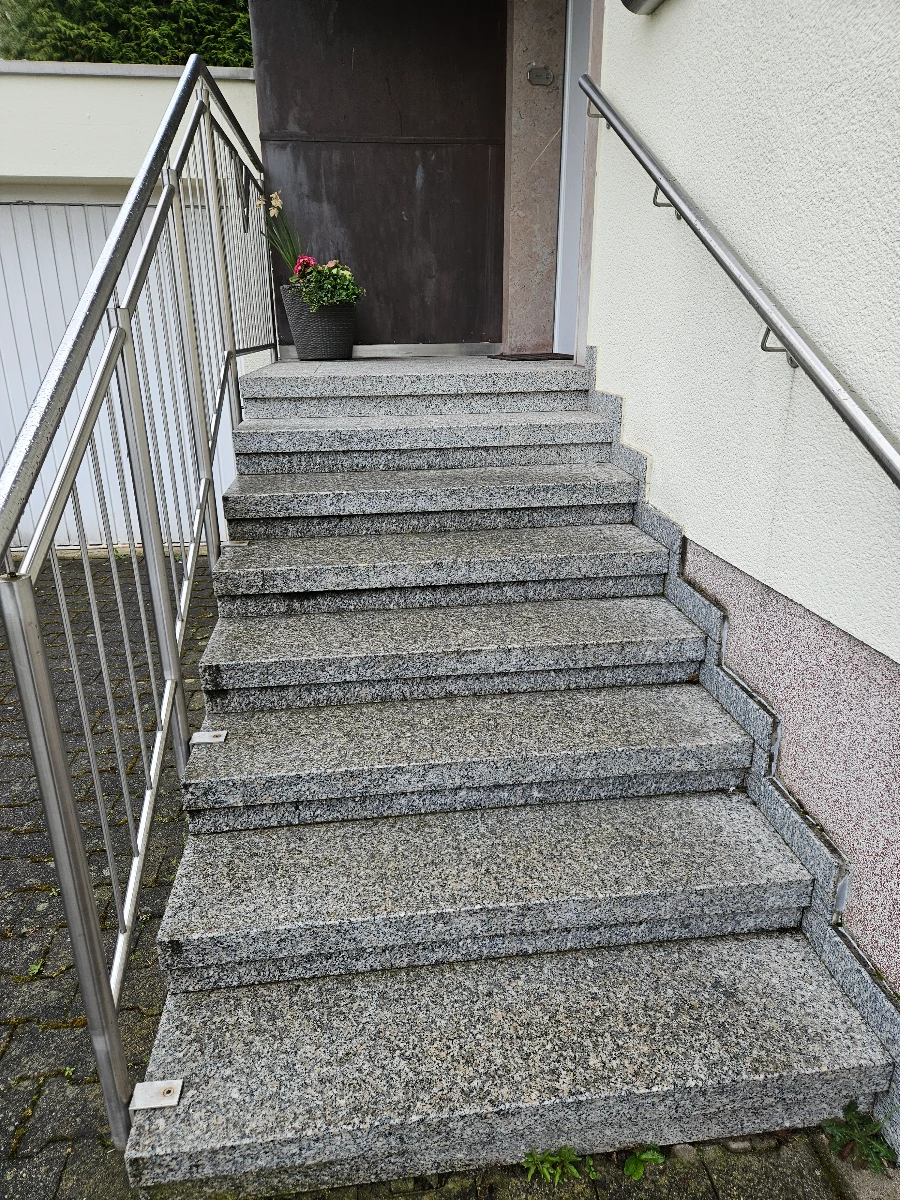 Aussenansicht einer grauen Granittreppe mit Edelstahlgeländer und Haustür – Dienstleistung Reinigung pflastersteine