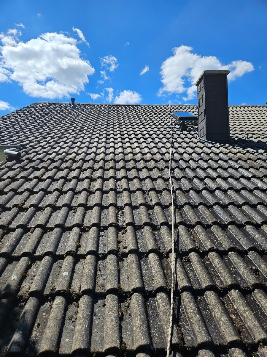 Schmutziges Ziegeldach mit Moosbefall und Schornstein unter blauem Himmel – Dachreinigung