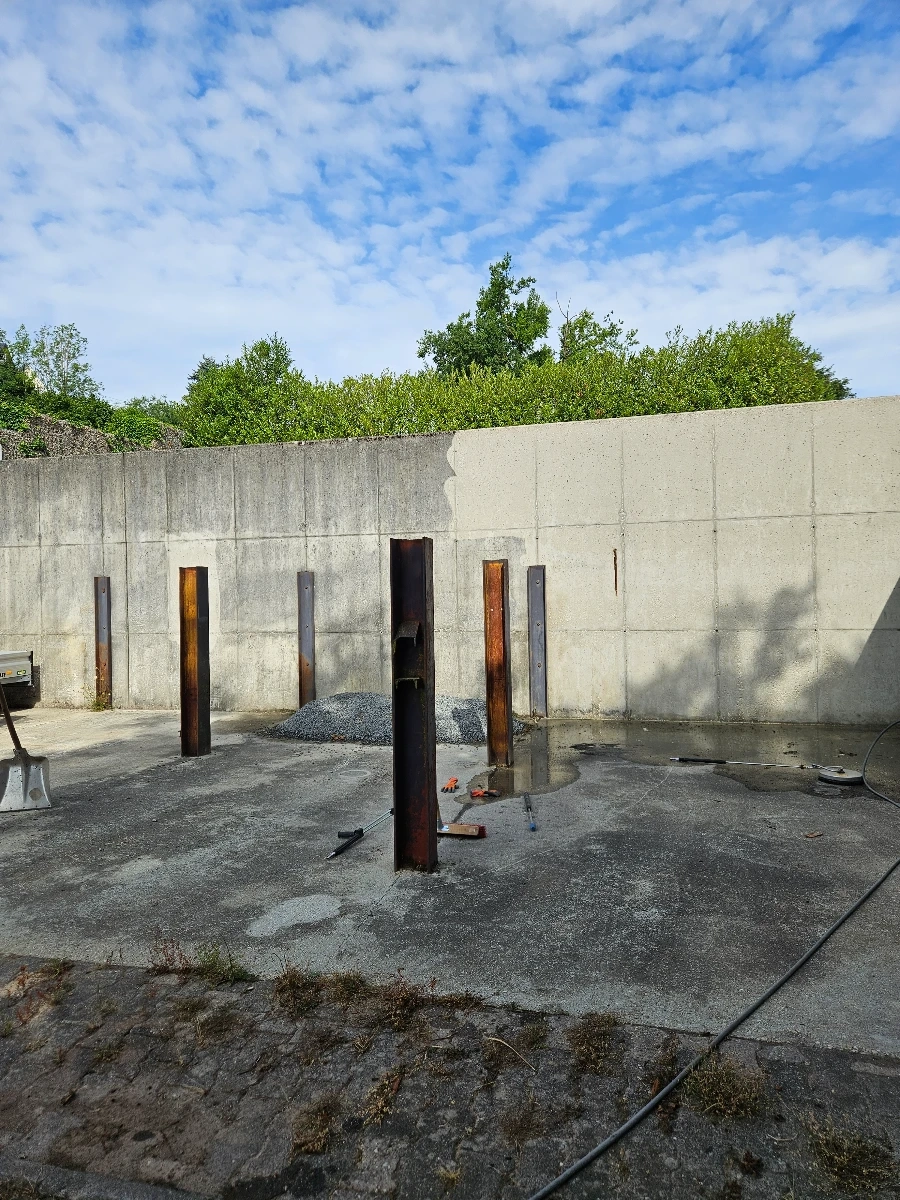 Verwitterte Betonfläche mit rostigen Metallpfosten vor Betonmauer für Hofreinigung