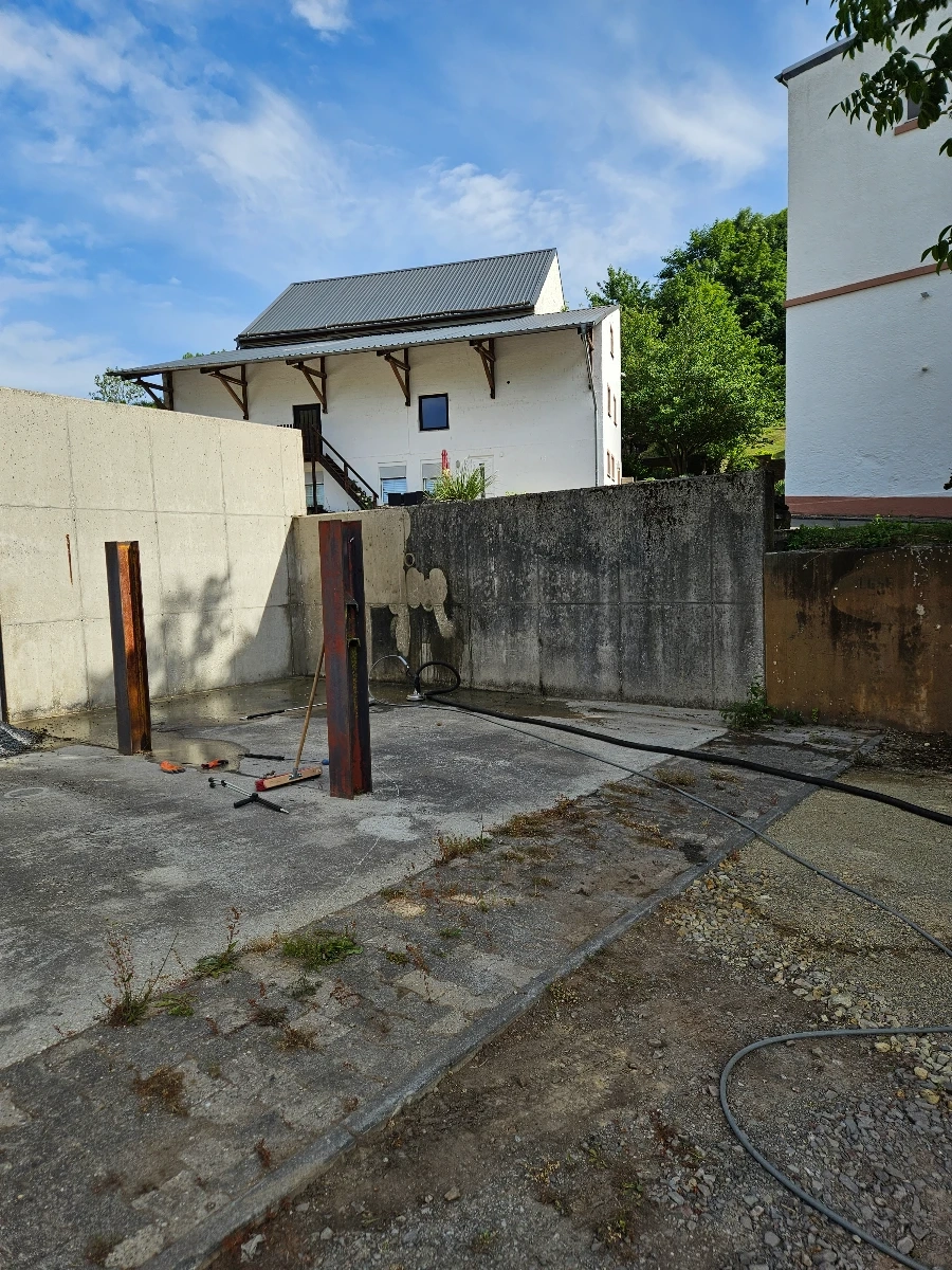 Hofreinigung: aufgebaute Reinigungsausrüstung mit Schläuchen und Metallpfosten auf gepflasterter Betonfläche