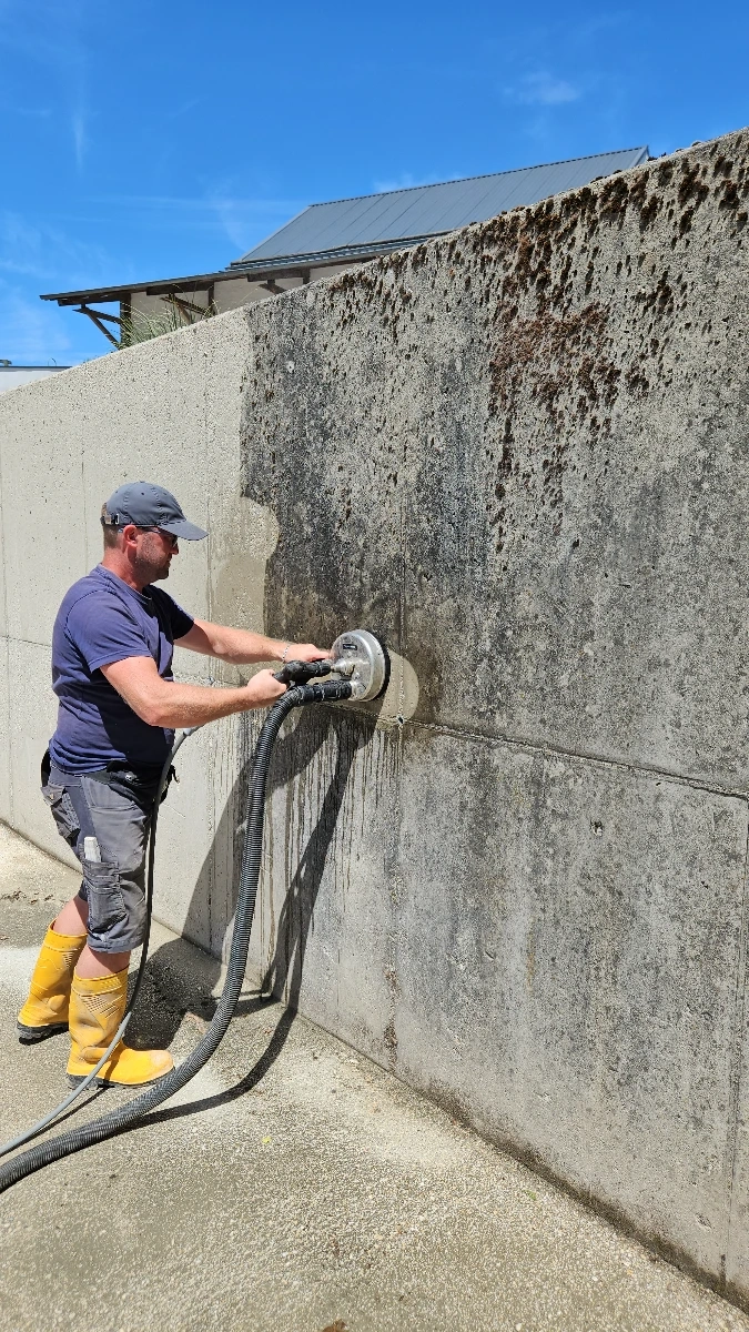 Arbeiter reinigt verschmutzte Betonwand mit rotierender Scheibenbürste unter hohem Druck – Fassadenreinigung