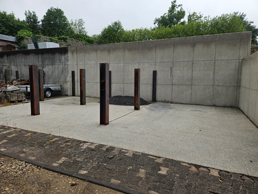 Betonhof mit hohen Betonmauern und rostigen Stahlpfosten, Hofreinigung