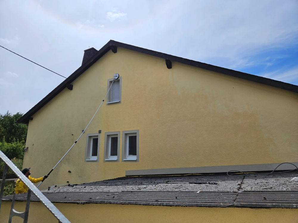 Person reinigt gelbe Hausfassade mit Teleskoplanze für Fassadenreinigung