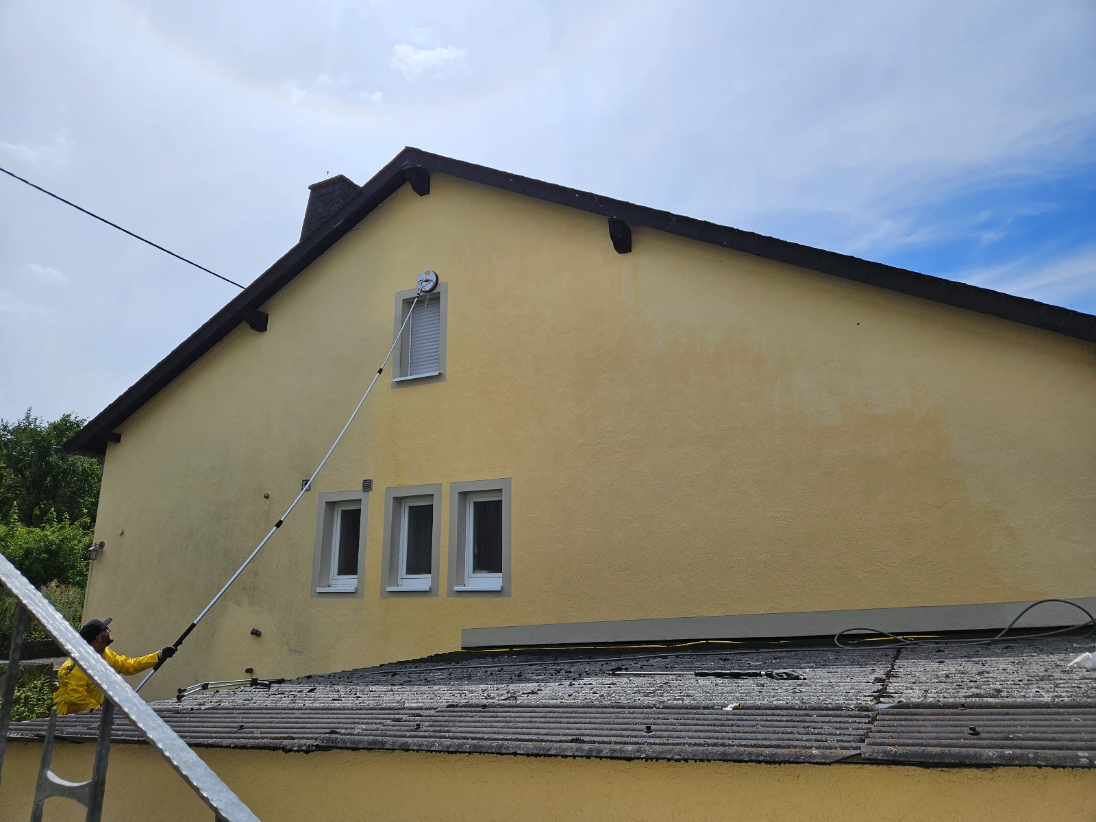 Fassadenreinigung mit Hochdrucklanze an gelber Fassade eines Einfamilienhauses