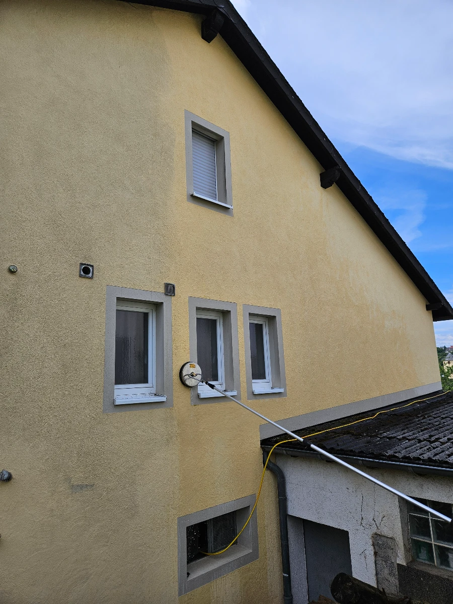 Gelbe Hausfassade mit Sauger und Teleskopstange bei Fassadenreinigung