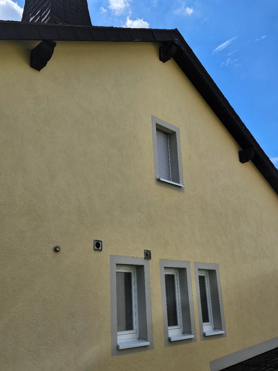 Gelbe Putzfassade eines Wohnhauses mit drei unteren und einem oberen Fenster, Fassadenreinigung