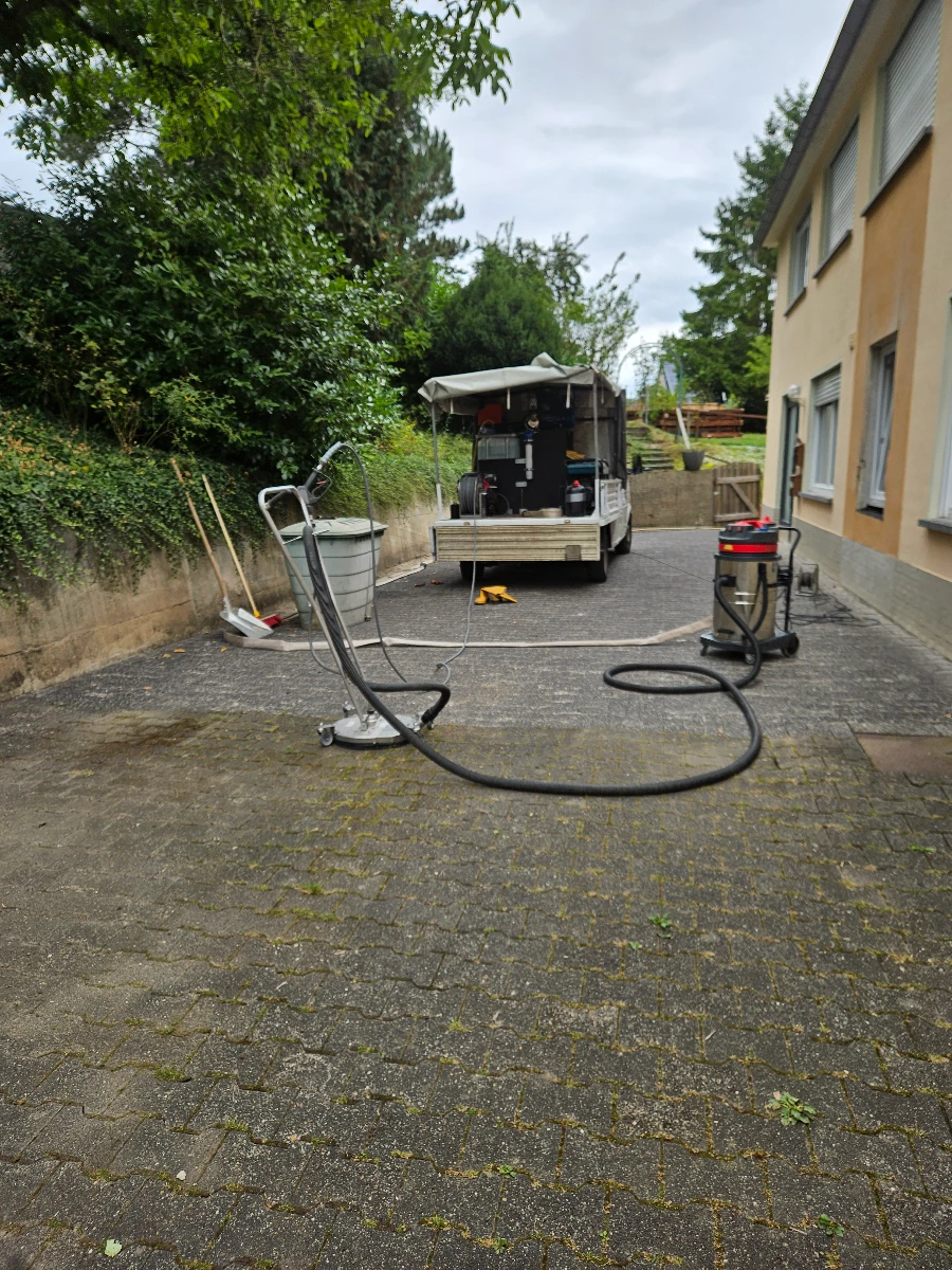 Mobiles Reinigungsequipment bei Reinigung pflastersteine auf gepflastertem Hof mit Schlauch und Maschine