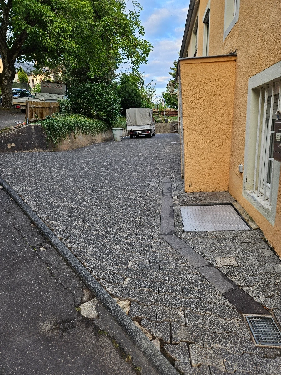 Schräger Einfahrtbereich mit grauen Pflastersteinen vor gelber Hausfassade – Reinigung pflastersteine