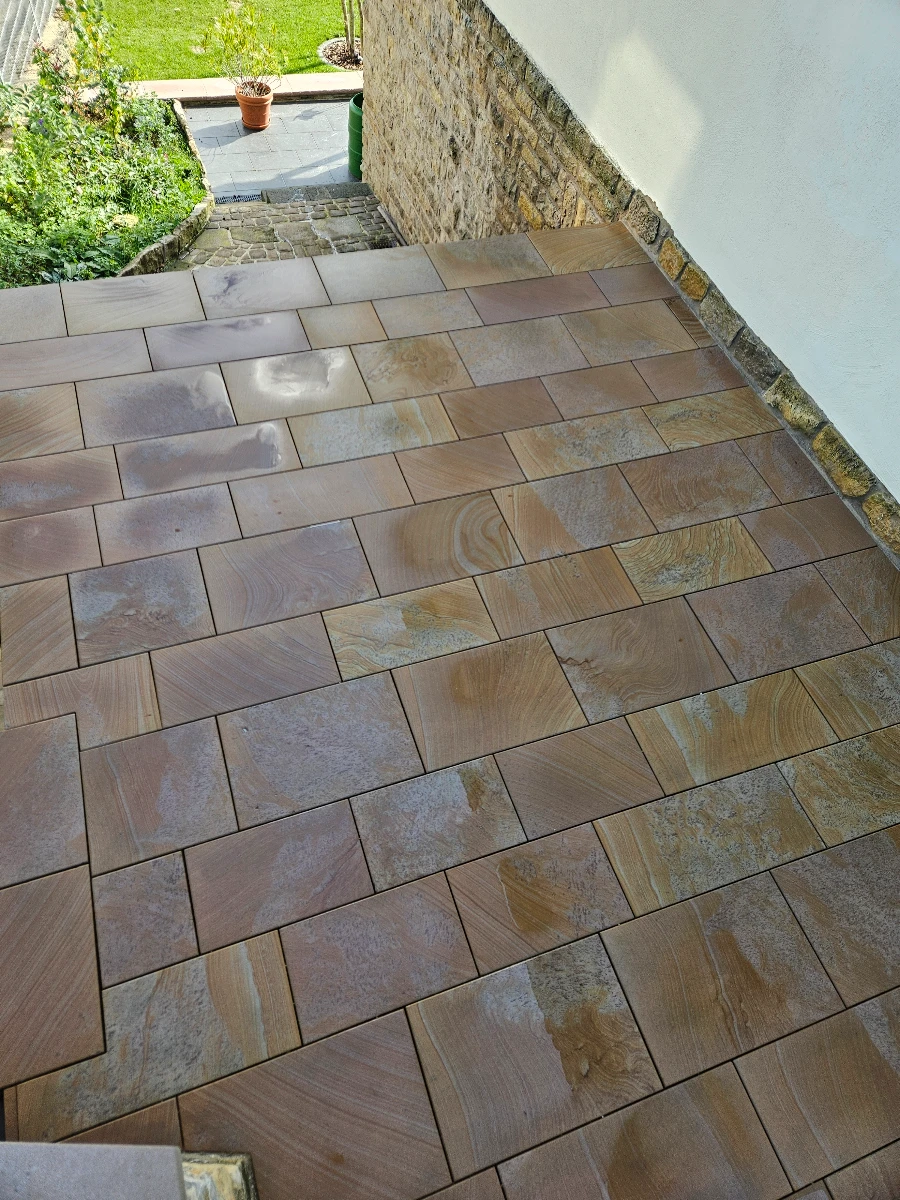 Blick auf helle, frisch gereinigte Sandsteinplatten einer Terrasse an Hauswand mit Treppenaufgang und Topfpflanze – Terrassenreinigung