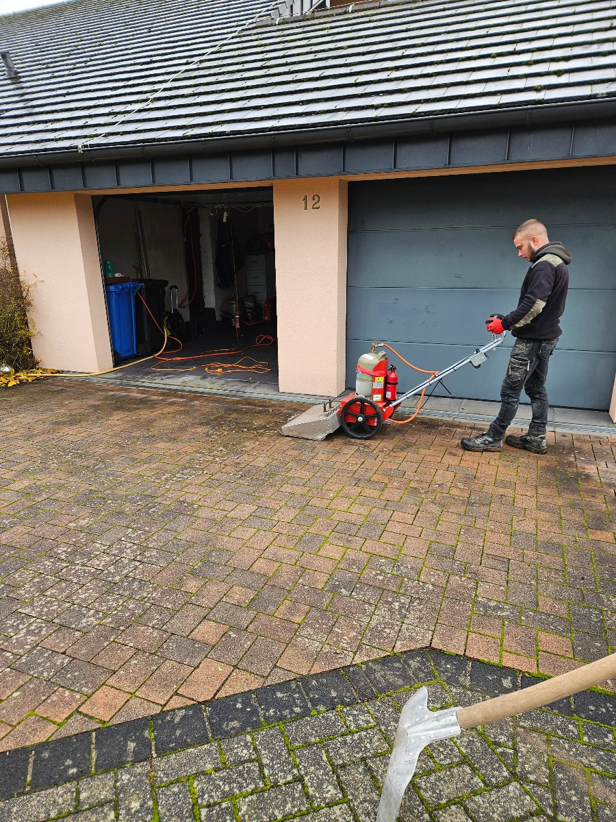 Mitarbeiter bei der Reinigung pflastersteine eines Einfahrts mit mobilem Hochdruckgerät vor Garage