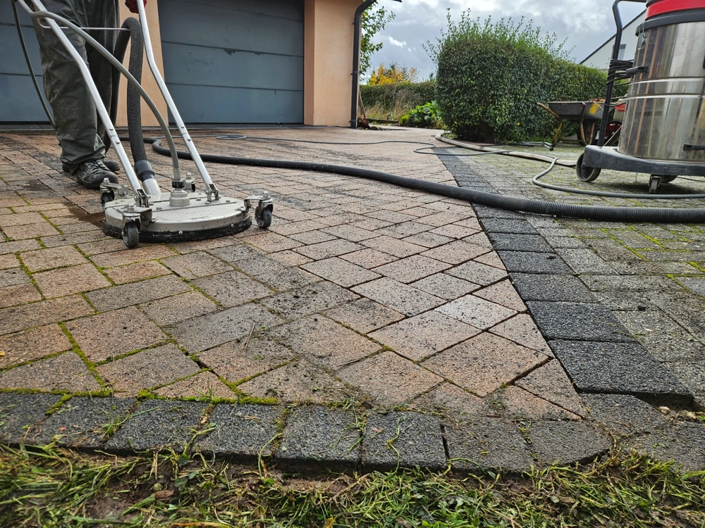 Mitarbeiter reinigt mit Hochdruck-Flächenreiniger verschmutzte Pflastersteine einer Einfahrt Reinigung pflastersteine