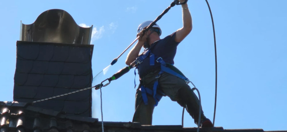Handwerker mit Hochdrucklanze säubert Dachfläche am Schornstein zur Dachreinigung