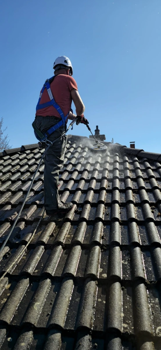 Handwerker mit Helm und Sicherheitsgeschirr säubert Dachziegel mit Hochdruck – Dachreinigung