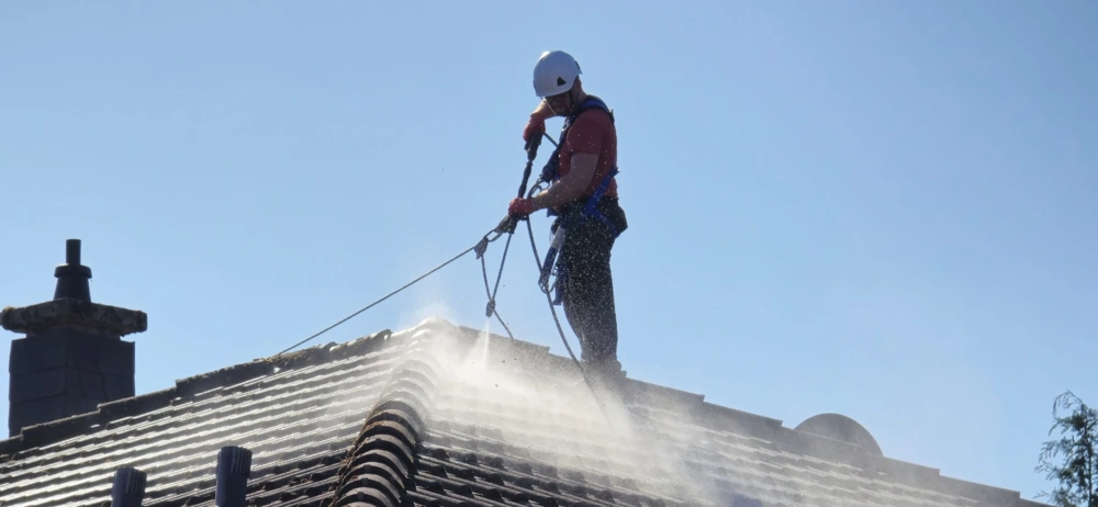 Arbeiter mit Helm und Sicherung bei der Dachreinigung von Ziegeln per Hochdruckreiniger