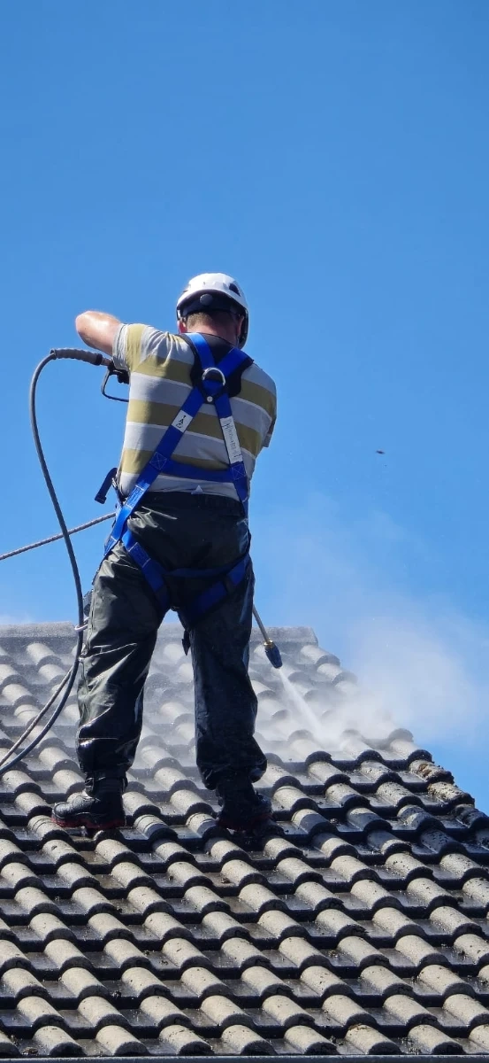 Handwerker auf Ziegeldach mit Hochdruckreiniger bei der Dachreinigung