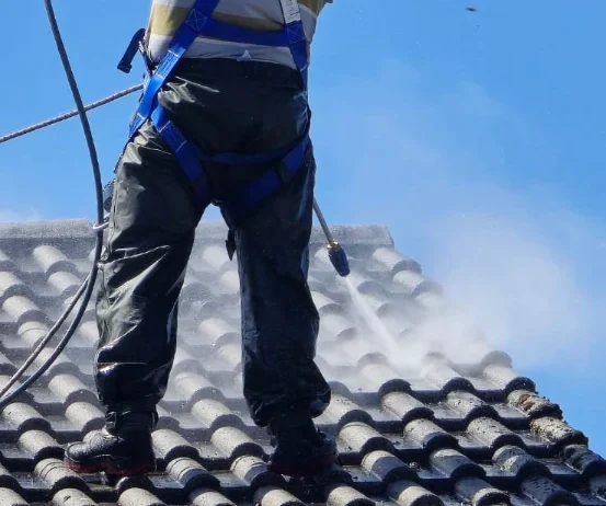 Dachreinigung: Handwerker entfernt Moos und Schmutz von Ziegeldach mit Hochdruckreiniger
