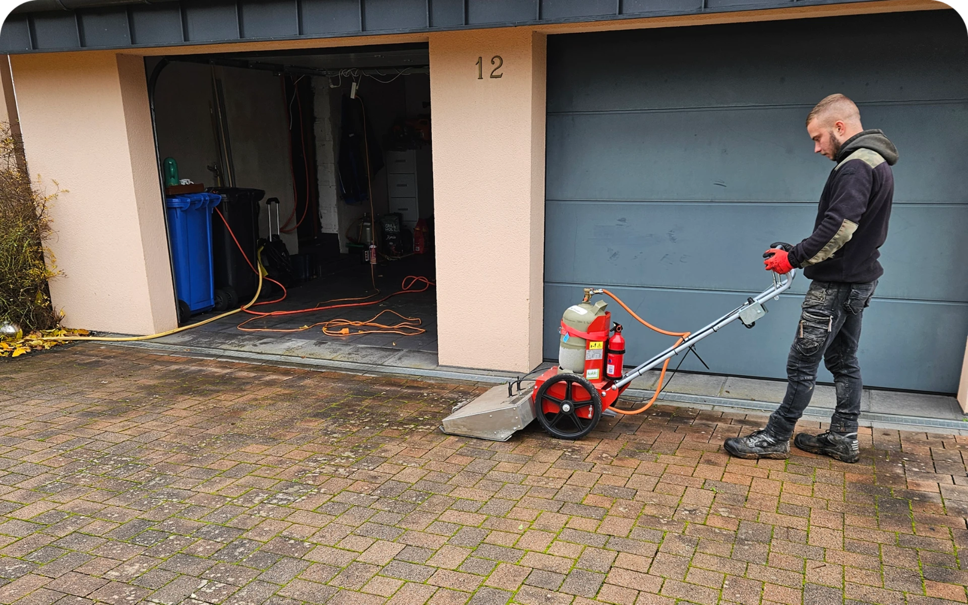 Hofreinigung auf gepflasterter Einfahrt mit professionellem Hochdruckgerät durch Mitarbeiter