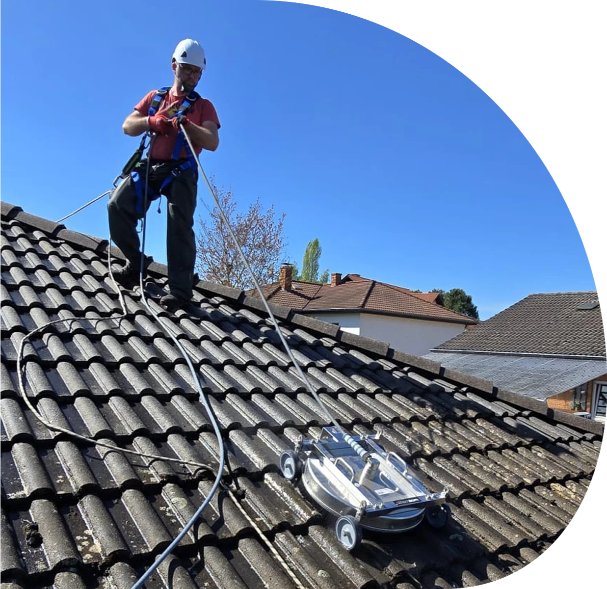 Gesicherter Mitarbeiter auf Ziegeldach bei Dachreinigung mit mobiler Reinigungsmaschine