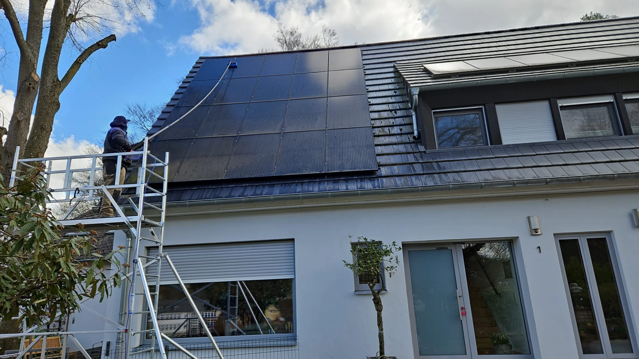 Handwerker auf Gerüst reinigt Solarpanels mit Niederdruckgerät bei Solarreinigung